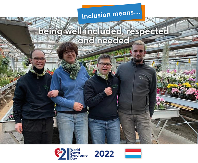 Two young men with Down syndrome are standing next to/between two colleagues in the greenhouse of a garden centre.