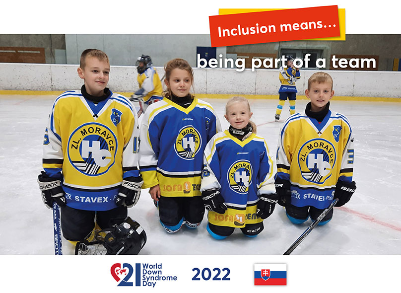 For a photo, a little ice hockey player with Down syndrome has joined her siblings on the ice of a stadium. They are all wearing their team uniforms and sports gear.