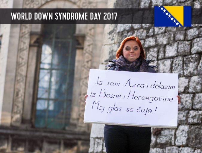 Young lady with Down syndrome standing in front of a church and holding up a poster with a statement.