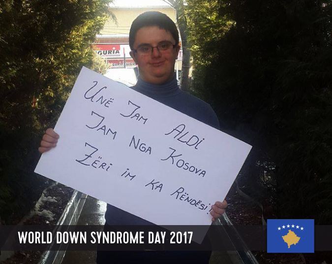 Young male person with Down syndrome holding a sign with his statement in front of his chest.