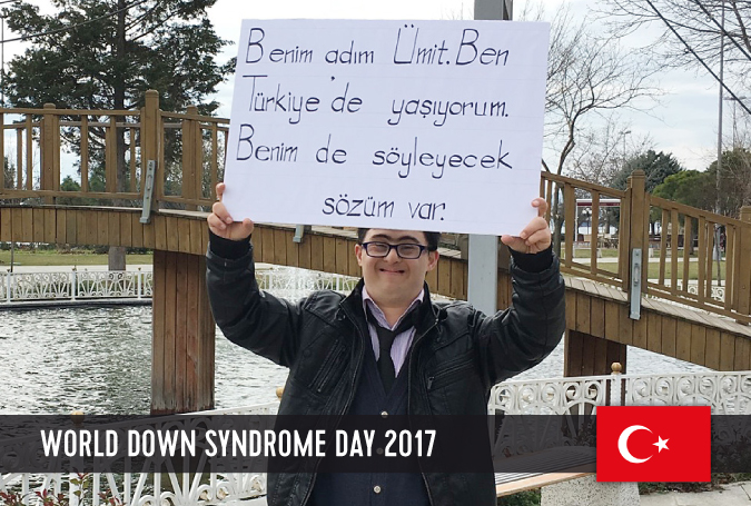 Young man with DS from Turkey holding a sign with his statement on WDSD 2017 above his head.