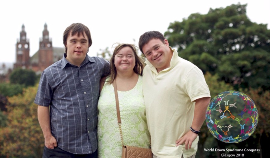 Three young people with Down syndrome, standing in front of some trees. with a church in the background.
