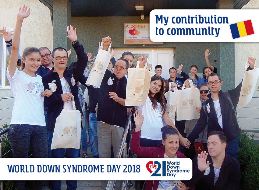 The group of volunteers - young women and men with and without Down syndrome - in front of the entrance to their club house. They wave, some with a textile bag advertising an educational program, in their hands.