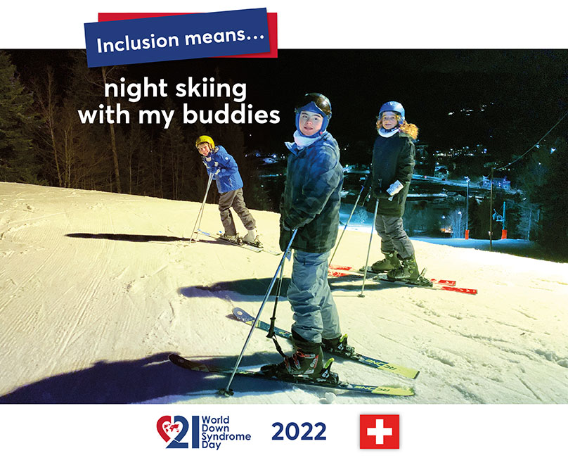 Three young skiers (one with a DS in the middle) stand in the floodlight of a ski slope illuminated at night and look into the camera. The lights of a town can be seen in the dark background.